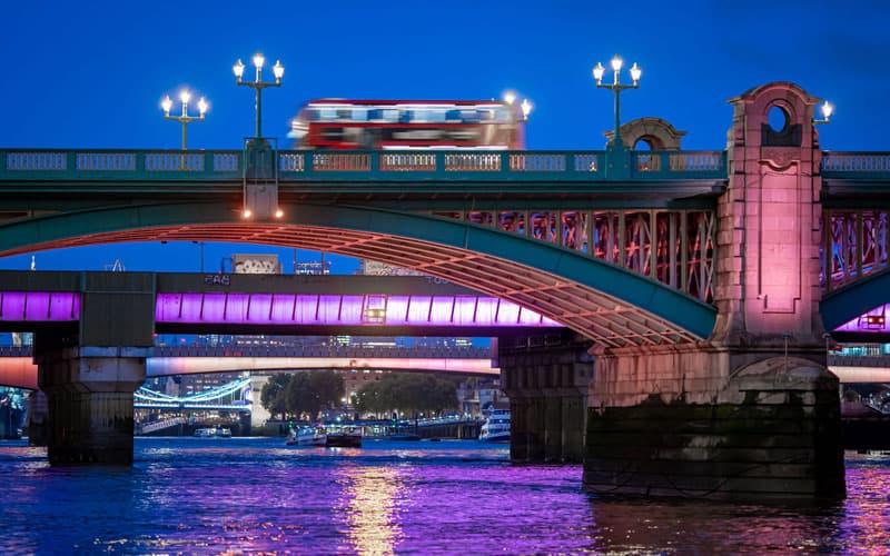夜色中，一辆模糊的红色双层巴士行驶在泰晤士河上的一座桥上.